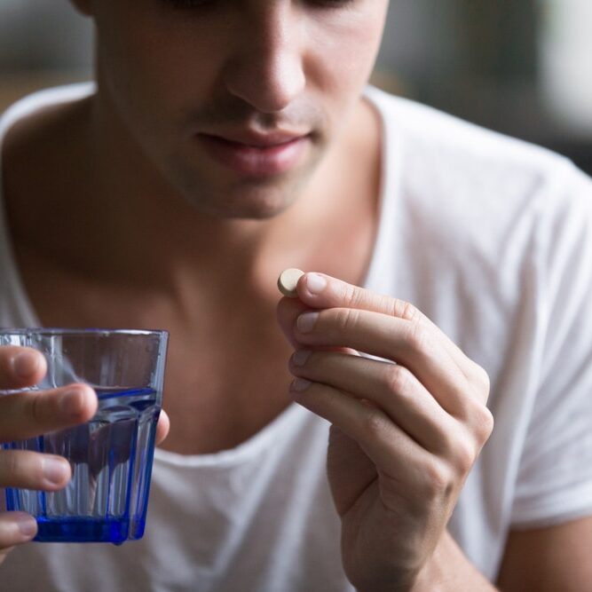 Sick,Ill,Depressed,Man,Holding,Glass,Of,Water,Taking,Pill